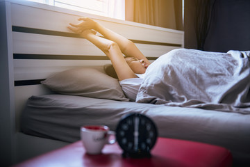 Asian woman wake up stretch oneself and yawn on her bedroom with blur black alarm clock