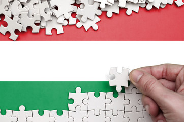 Hungary flag  is depicted on a table on which the human hand folds a puzzle of white color