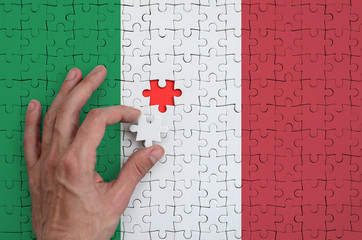 Italy flag  is depicted on a puzzle, which the man's hand completes to fold