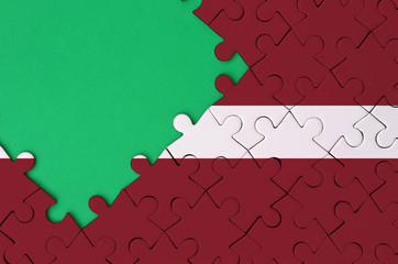 Latvia flag  is depicted on a completed jigsaw puzzle with free green copy space on the left side