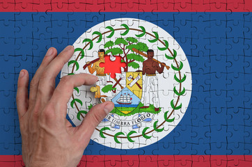 Belize flag  is depicted on a puzzle, which the man's hand completes to fold