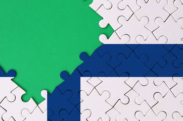 Finland flag  is depicted on a completed jigsaw puzzle with free green copy space on the left side