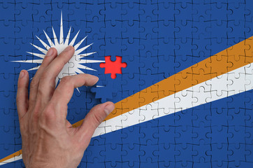Marshall Islands flag  is depicted on a puzzle, which the man's hand completes to fold