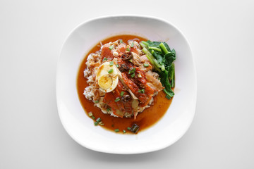 rice with crispy pork, red pork, sausage, roasted duck, boiled egg, vegetable and red sauce on white dish and table is traditional thai chinese food for lunch at restaurant or food court on top view