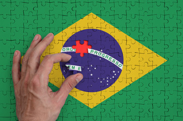 Brazil flag  is depicted on a puzzle, which the man's hand completes to fold - Powered by Adobe