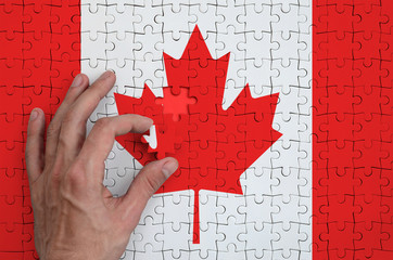 Canada flag  is depicted on a puzzle, which the man's hand completes to fold