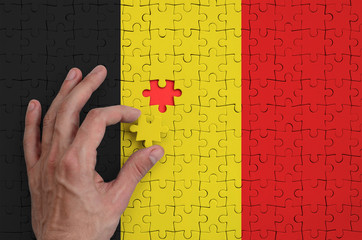 Belgium flag  is depicted on a puzzle, which the man's hand completes to fold
