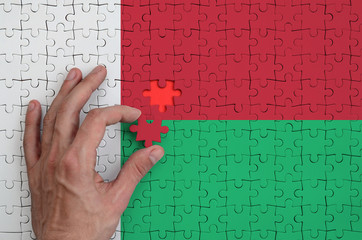 Madagascar flag  is depicted on a puzzle, which the man's hand completes to fold