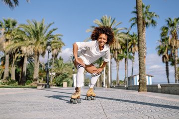 Black woman on roller skates rollerblading in beach promenade with palm trees