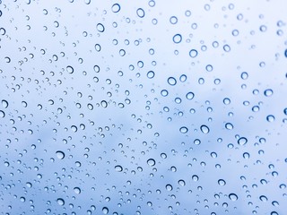 The raindrops on the windscreen or windshield or car glass. View from the inside of the car with a grey sky background. It can be use for texture background or display or backdrop. Adjust the image to