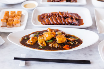 Deep fried snapper fillets stir fried with black pepper, onion, bell pepper, carrot and XO sauce with BBQ Pork and Crispy Pork Belly in background.