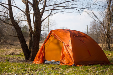 An orange tent built on the bank of the river. Hiking camp in the spring. Early spring scenery.