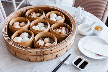 Dim sum set: Barbecued pork bun, Shrimp dumpling, Sweet cream buns, Shrimp shumai topping with goji berry served in steamer baskets with plate, chopsticks, sour sauce and hot tea.