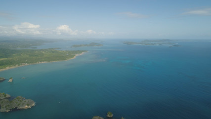 Aerial view of Groups islands with sand beach and turquoise water in blue lagoon among coral reefs, Caramoan Islands, Philippines. Mountains covered with tropical forest.