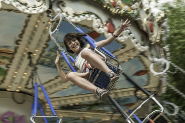 Fototapeta na wymiar Closeup of exhilarated young girl riding very fast on an amusement park swinging carousel with main subject slightly out of focus to depict speed