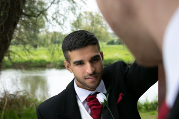 Gay couple of grooms pose for photographs by a lake on their wedding day