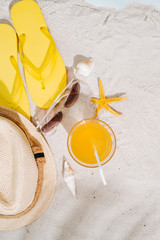 Fototapeta na wymiar Summer background. Beach accessories flip flops, sunglasses, hat and orange juice on sand background