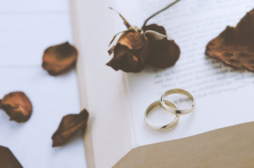 Couple wedding rings with dry roses at opened book
