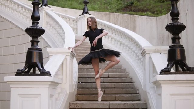 Slow motion of a young blonde girl in tutu standing on a beautiful white stairs outside on the street. Posing, practicing ballet movements