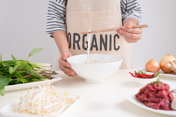 Female chef prepare traditional Vietnamese soup Pho bo with herbs, meat, rice noodles