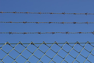 A barbed metal wire and fence against the blue sky 1