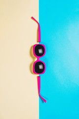 Studio shot of pink sunglasses. Summer is coming concept. Minimal style, minimalist photography. Top view of spread sunglasses on colorful paper backdrop. Yellow and blue pastel colors.