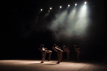 A group of small ballet dancers rehearses on stage with light and smoke