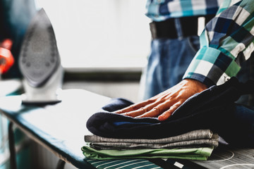 Man at home ironing clothes. Father performs home duties, irons the child's clothes. Man in role of a woman at home. Man ironing shirt on ironing board with steaming blue iron.
