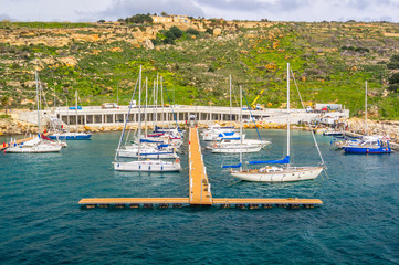 MGARR, GOZO, MALTA - FEBRUARY 02, 2013 - View of boats in the harbour with apartments on the hillside to the rear and people going about their business.