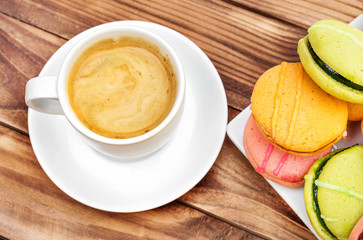 Cup of coffee with colorful macaroons on the wooden table. Top view.