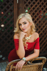 Fashionable attractive blonde woman in red dress sitting on chair.