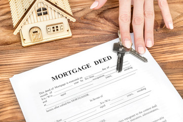 Female's hand giving mortgage deed and keys from house over table. Real estate concept.