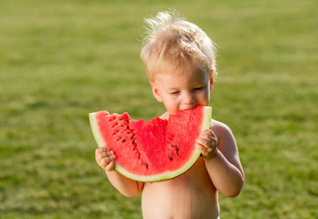 One year old baby boy eating watermelon in the garden