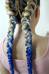 two braids on the head of a girl with a kanekalon, thick braids in her hand, close-up on a white hair dryer, colored hair woven into a braid, build-up of artificial strands