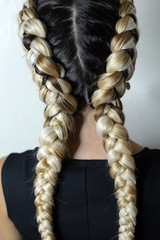 two braids on the head of a girl with a kanekalon, thick braids in her hand, close-up on a white hair dryer, colored hair woven into a braid, build-up of artificial strands