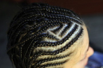 pigtails braided on the head, thin corn rows, African style hairstyles for girls close-up work of the master
