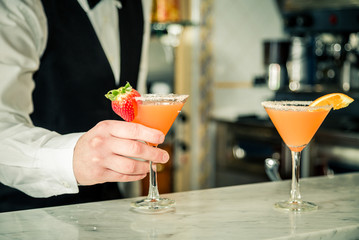 Bartender's hand serving a cocktail. Two orange cocktails with fruit slices on the bar counter and  blurred background