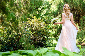Full length body portrait of beautiful bride in fashion wedding dress walking in the park outdoors, back view, copy space