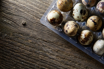 Quail eggs in a plastic container on a dark wooden background, top view, selective focus