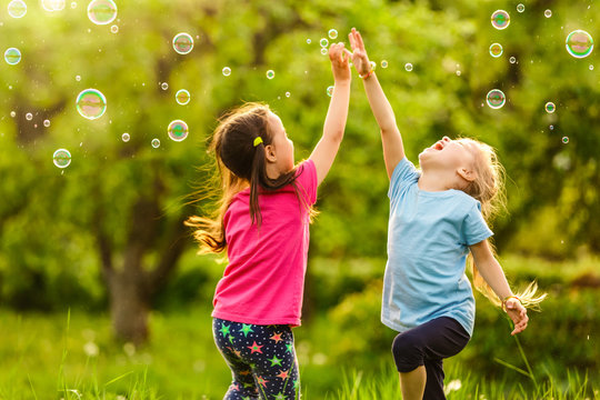 Two Little girl fun with soap bubbles in summer park, green fields, nature background, spring season