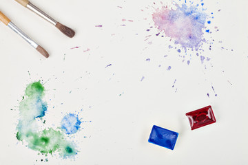 brush, paints and colored watercolor blots on paper on white background