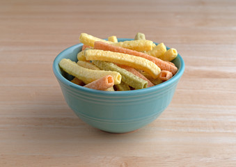 Veggie straws in a green bowl on a wood table.