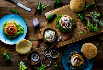 Chicken burgers with fresh salad, onion, peppers and mayonnaise sauce. Overhead view and dark, wooden background.