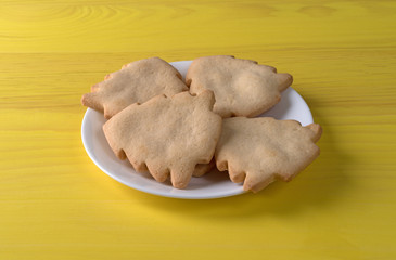 Fototapeta premium Tree shaped Christmas cookies on a white plate atop a yellow table.
