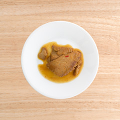 Tilapia fillet in sesame sauce on a plate atop a wood table.