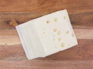 Several slices of low sodium Swiss cheese on wood a cheese board.