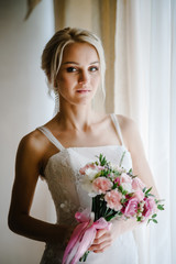 Stylish bride with a wedding bouquet of flowers near the window indoors in the rooms.