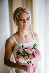 Serious portrait of bride with luxury make-up and hairstyle with a wedding bouquet of flowers, standing in studio indoor photo.