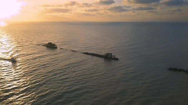 Vista aerea di sagome dei trabucchi sul mare per la pesca del pesce con pescatori alle ultime luci del tramonto.