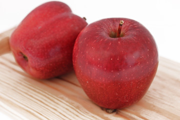 Dos manzanas rojas sobre tabla de madera, en fondo blanco 